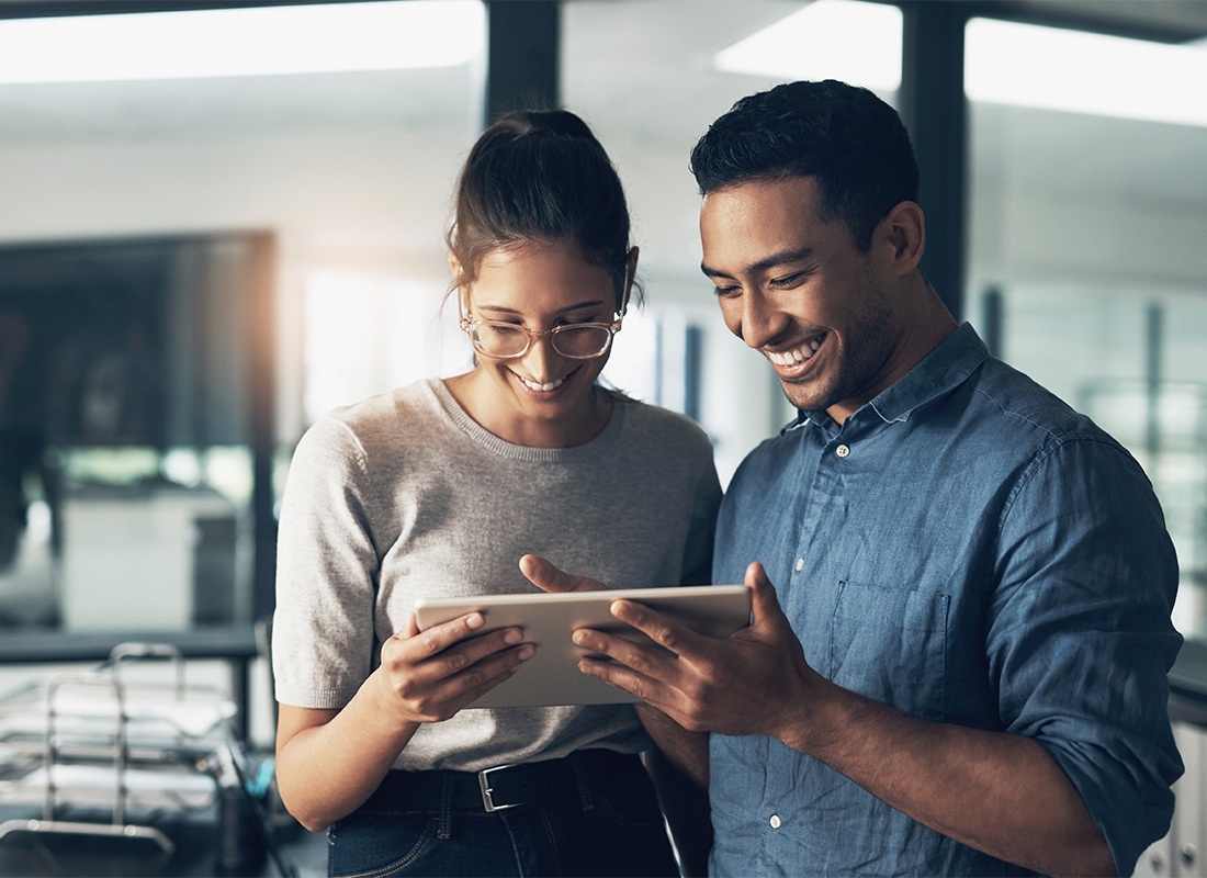 Employee Benefits - Portrait of Cheerful Young Male and Female Coworkers Looking at a Tablet While Standing in the Office