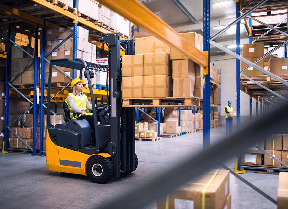 Insurance by Industry - View of a Young Female Warehouse Worker Riding a Forklift with Boxes in a Warehouse